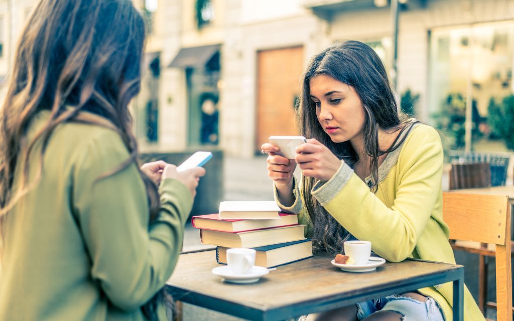 two women sit opposite each other glued to their phones looking at social media