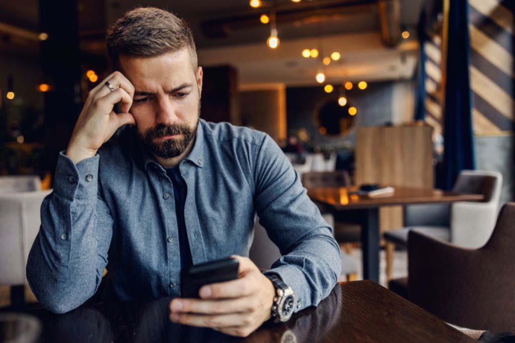 man looking more measured at phone in cafe