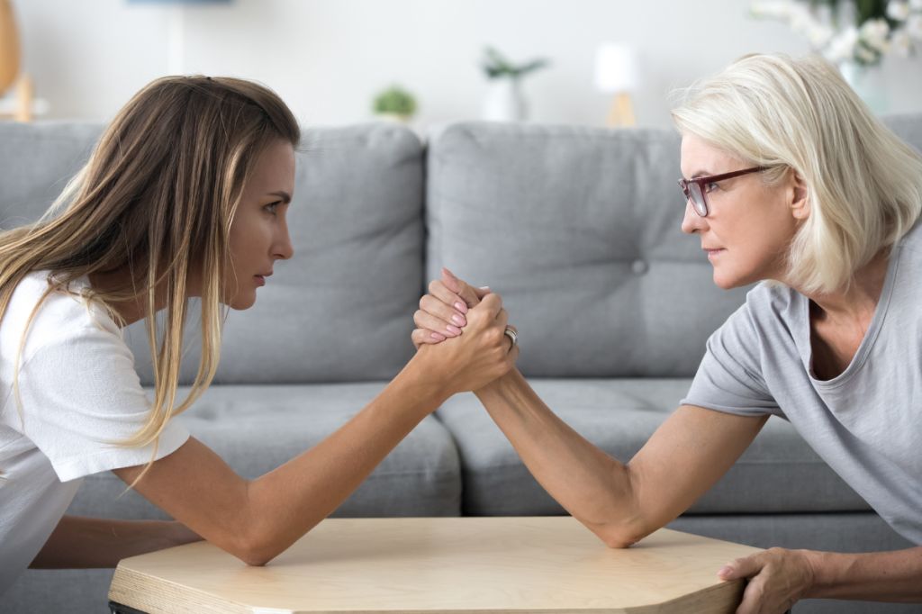 family conflict between pretty mother and daughter as they sit and arm wrestle on the sofa