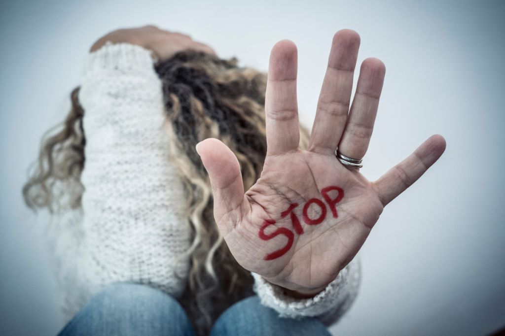 woman sat on floor with head in hands, one hand out with word stop written on it
