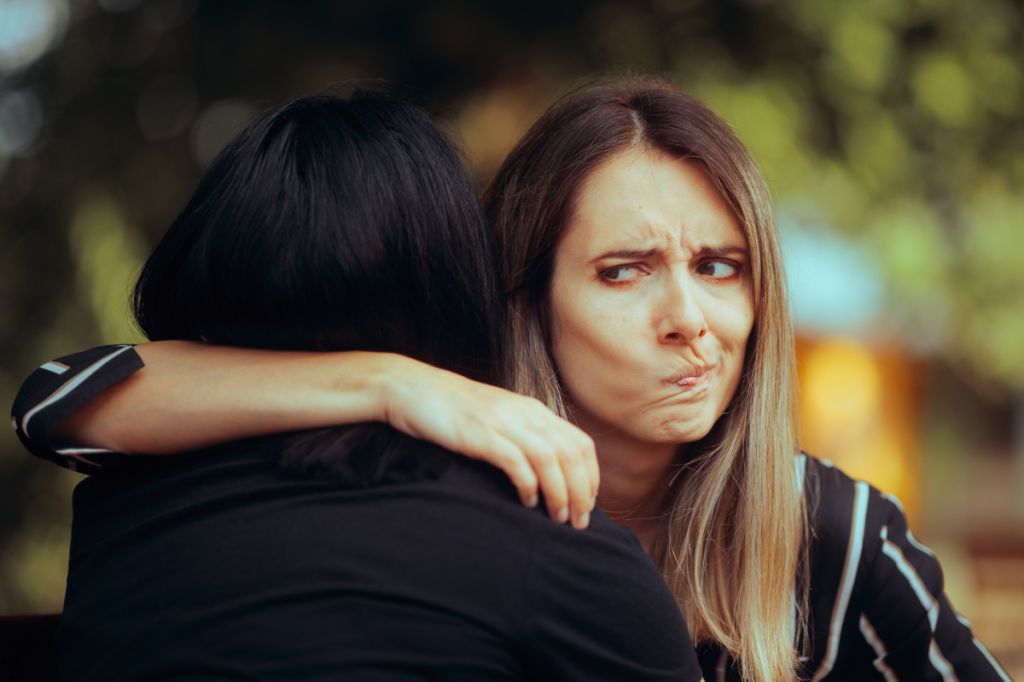 woman hugging friend but pulling unhappy face