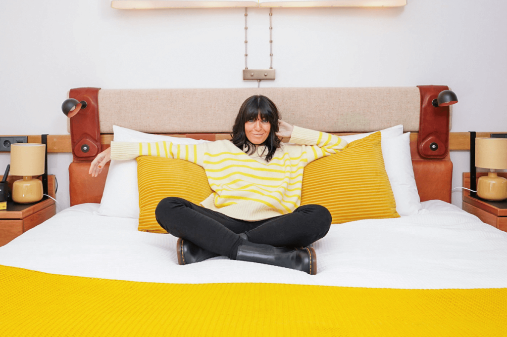 Claudia Winkleman sitting on a yellow bed in a yellow jumper