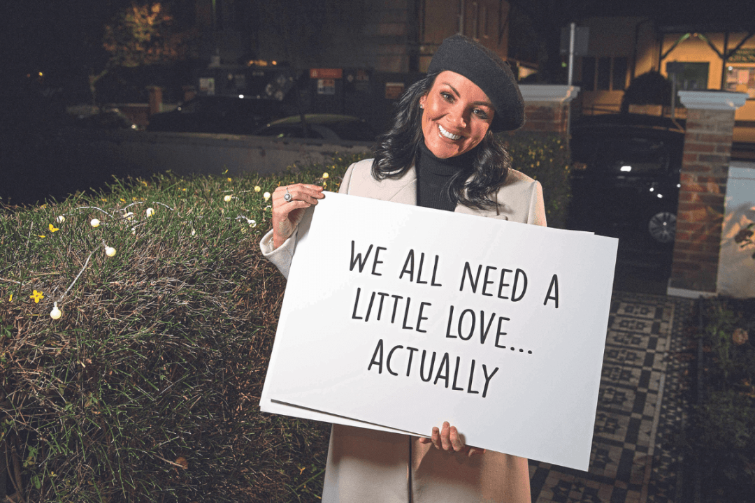Martine McCutcheon holding a paper sign that says 'We all need a little love... actually'
