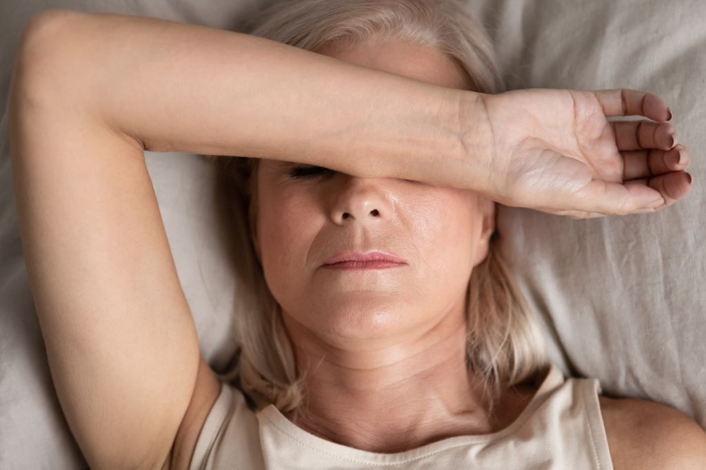 A woman on a bed covers her eyes with her forearm in fatigue