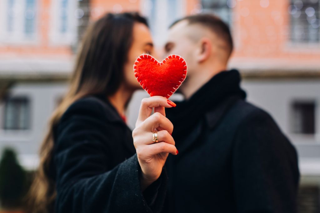 Couple kiss, faces obscured by red felt heart, strong chemistry