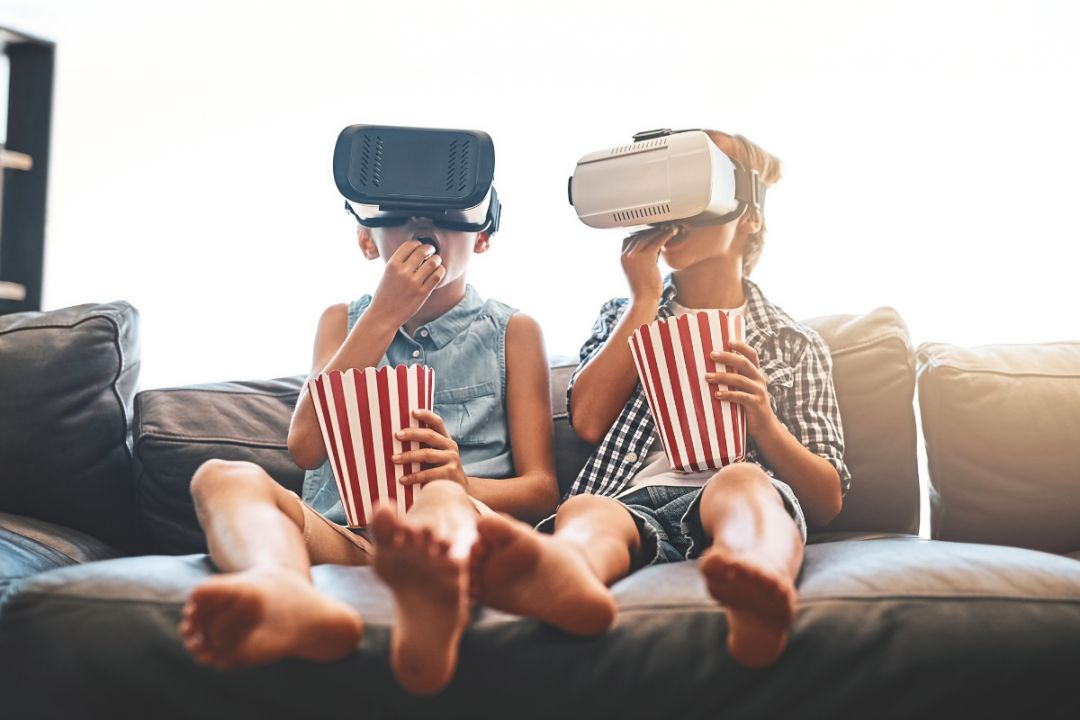 Two boys sit wearing VR masks and eating popcorn