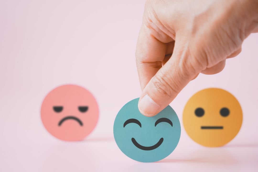 three paper faces, one sad, one neutral one happy. chant chooses happy face