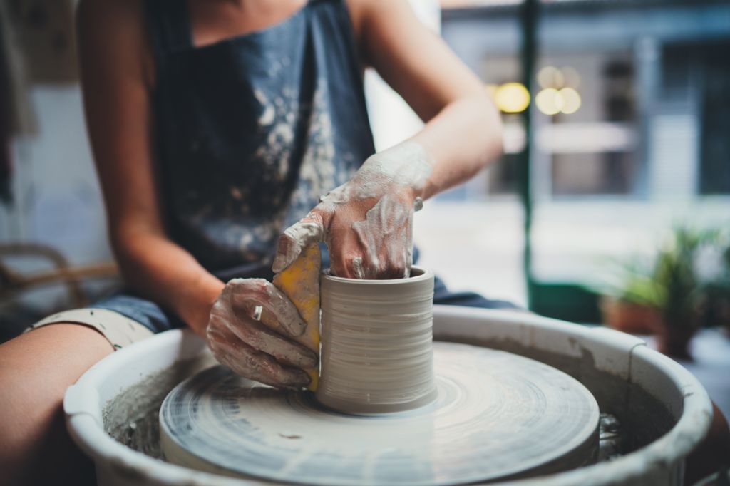 Potter sits at wheel with dirty hands making pot