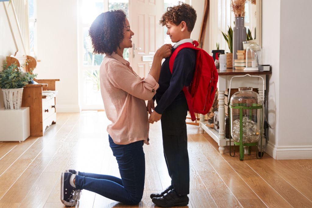 Mum kneels in front of child getting ready for school