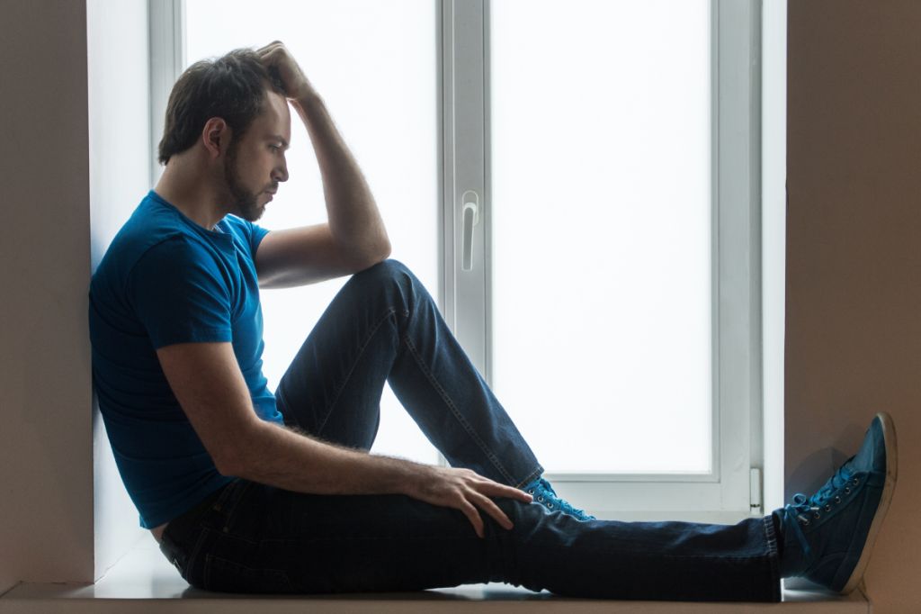 man in low mood looks sits looking out of window