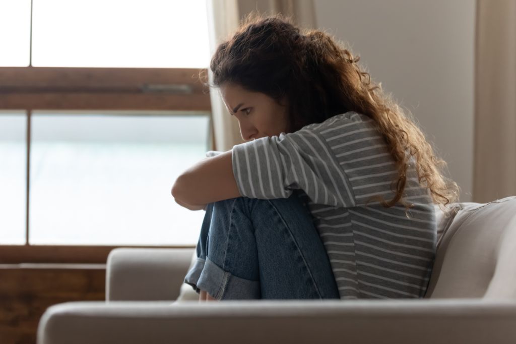 woman sits on sofa with knee up looking tired and anxious