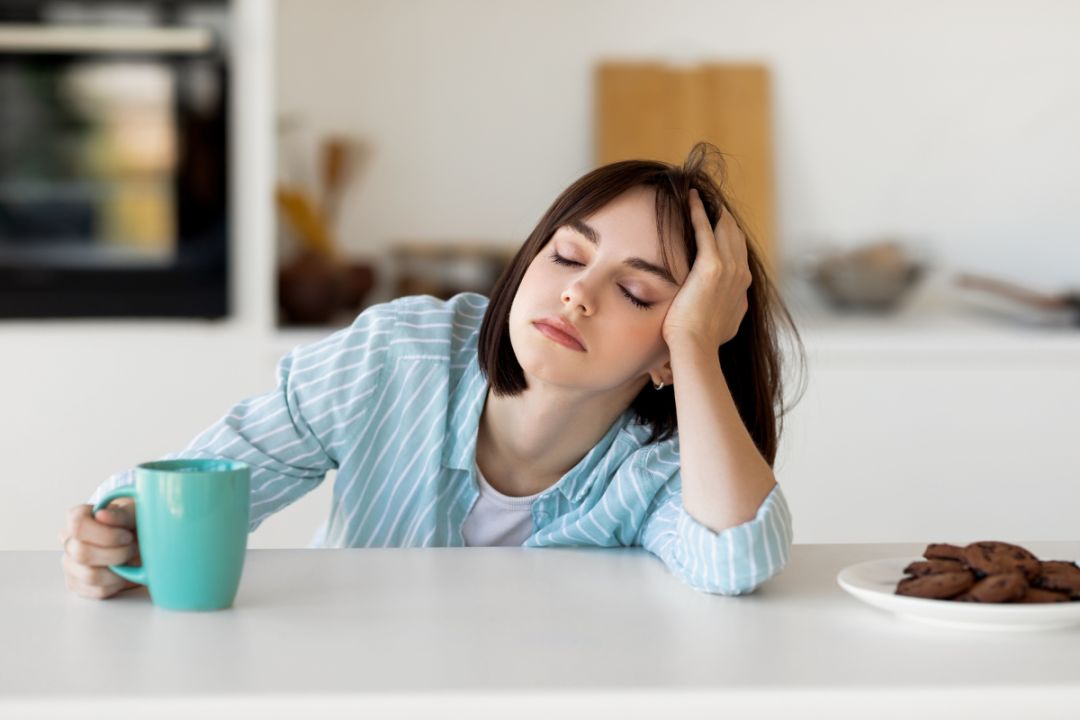Tired woman sits with coffee with eyes closed