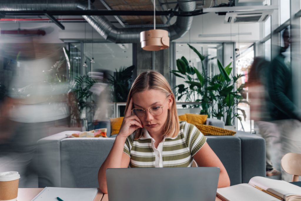 Woman sits at desk in office surrounded by blur of people