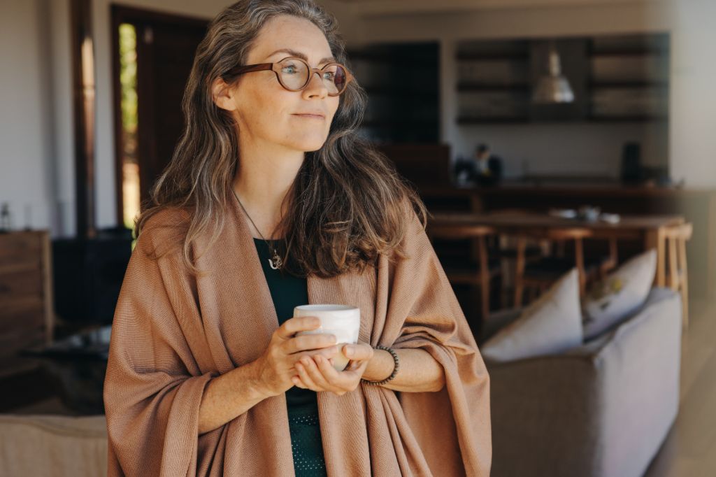 woman holds cup of coffee wrapped in a blanket looking relaxed and happy