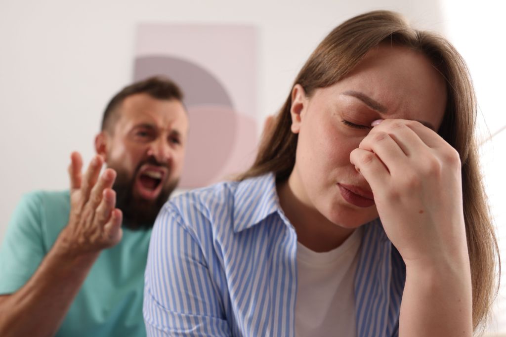 man screaming at woman, she holds head
