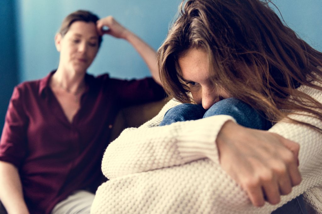 woman looks on smugly as younger woman looks upset