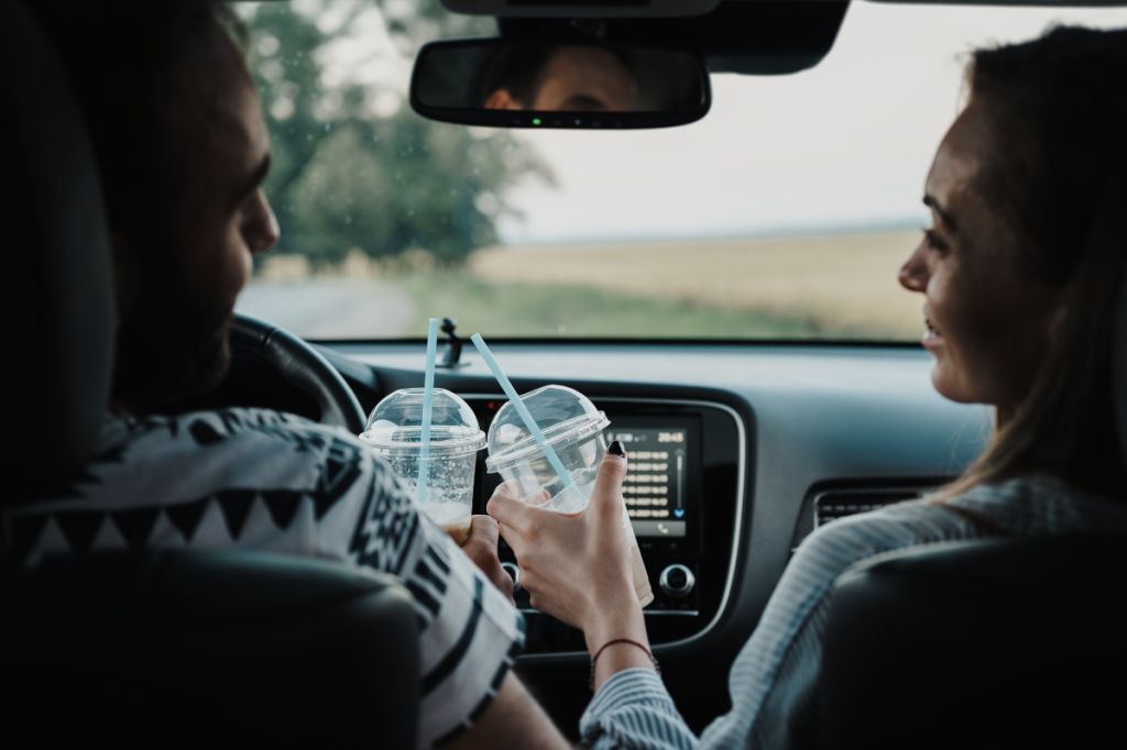 couple clink plastic drinks cups in car
