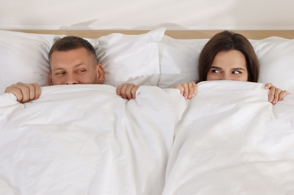 couple lying in bed looking excitedly at each other