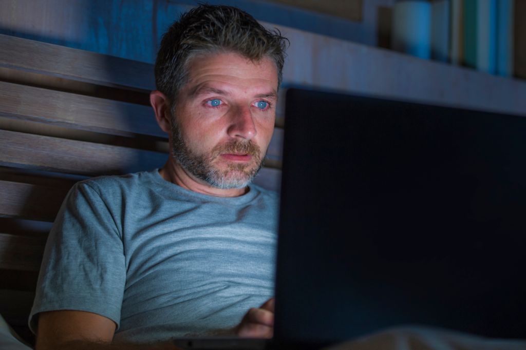 man sat in bed in dark looking at computer