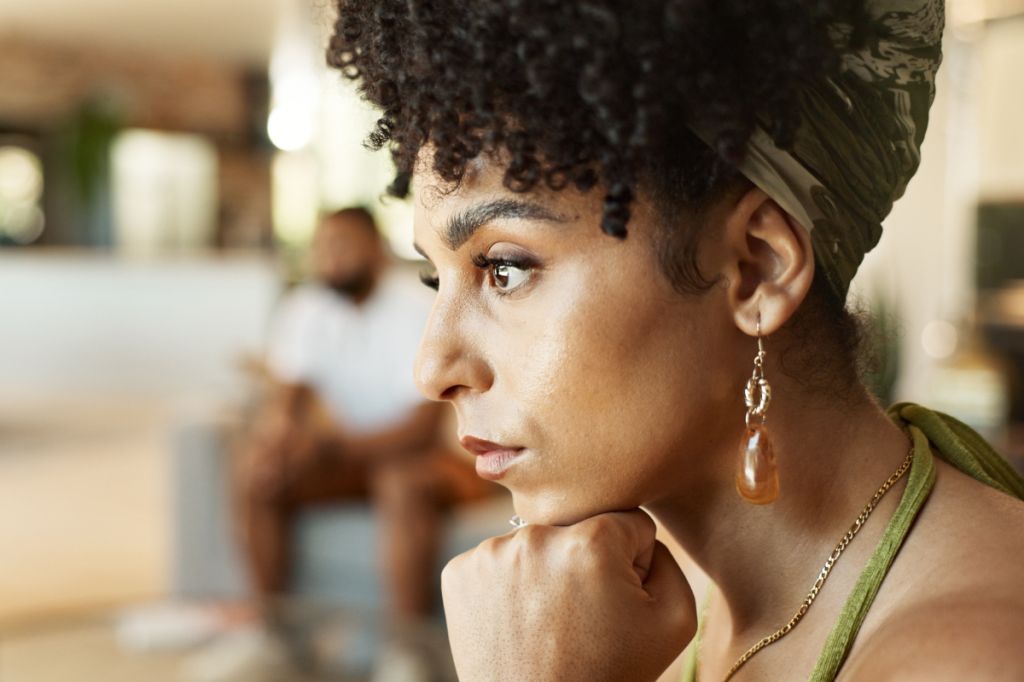 woman thinking with head on hands, partner in background