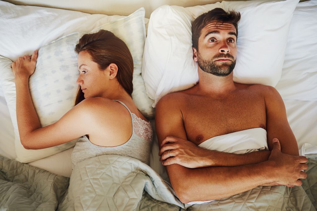 upset couple in bed, she looks sad he looks angry