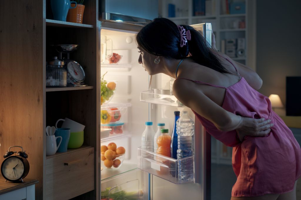 Woman looks into fridge in a dark kitchen