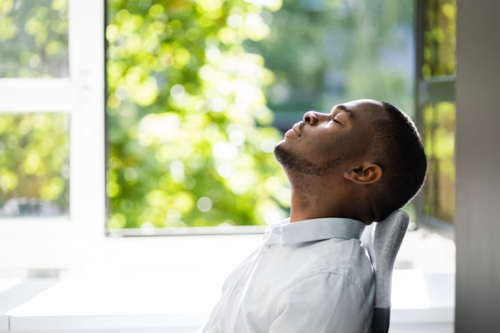 man sits at a desk and drops his head back as he takes a deep breath