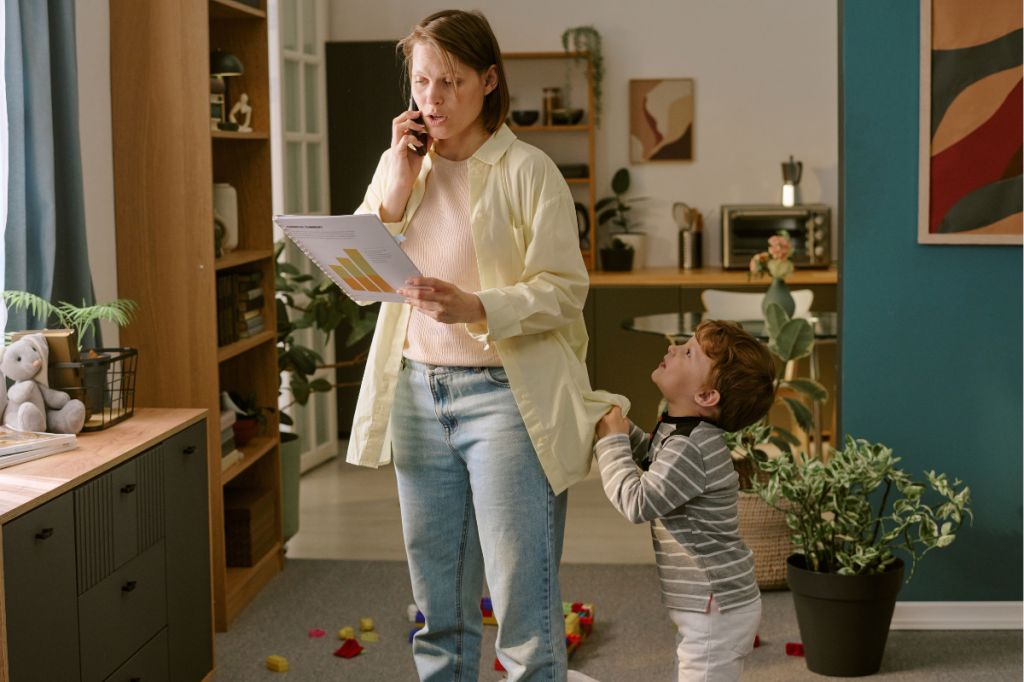 stressed mum looks at graphs and talks on phone, while young son begs for her attention