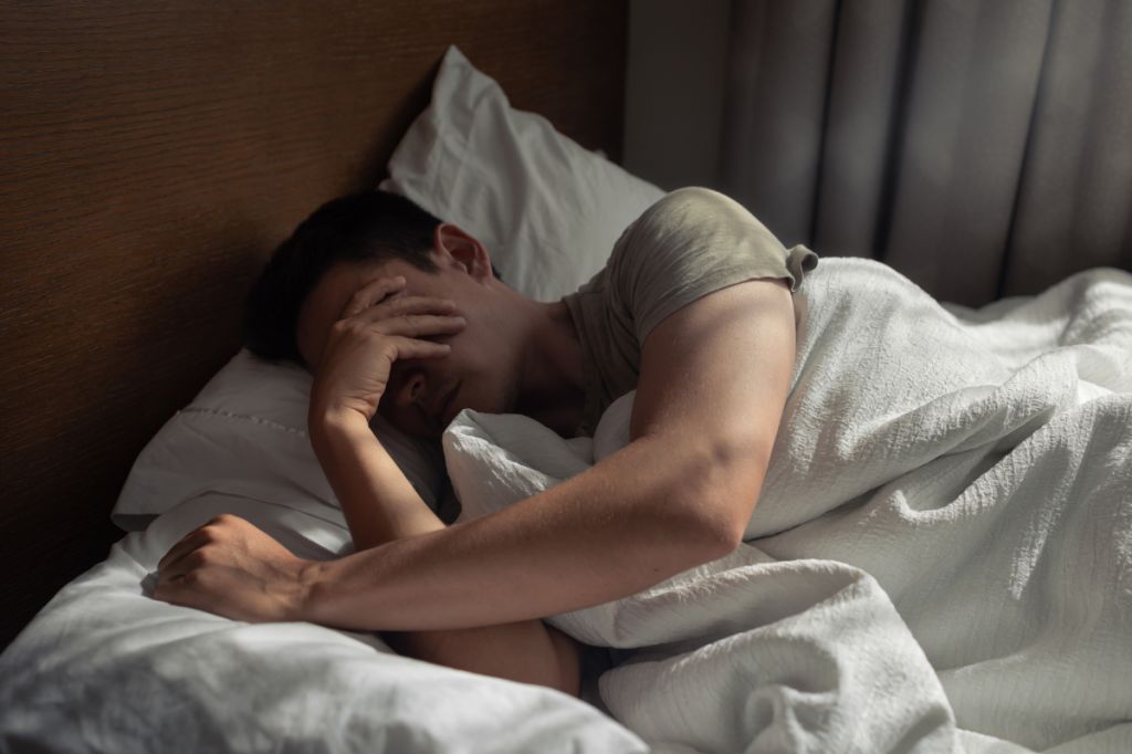 man lies in bed in dark covering eyes
