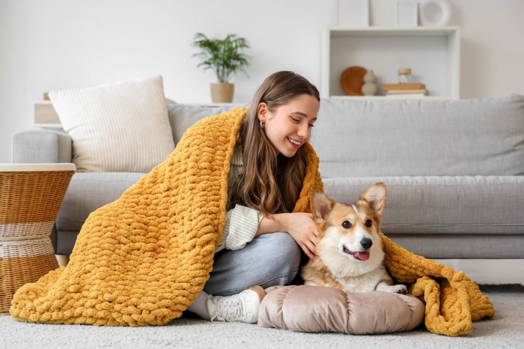 woman cuddles up under a blanket with corgi