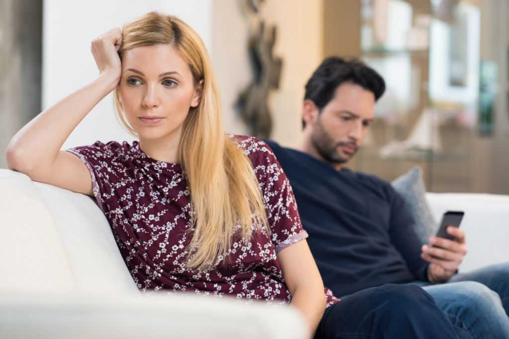woman looks away upset as man looks at his phone