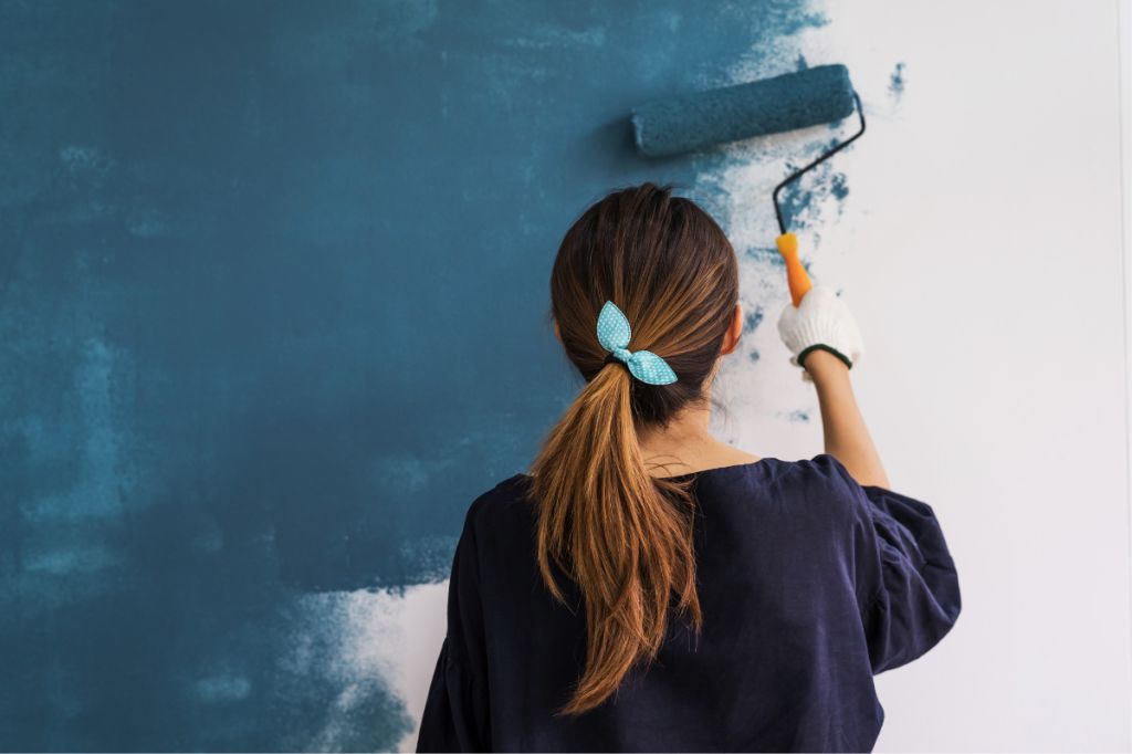 woman paints a wall blue with a roller