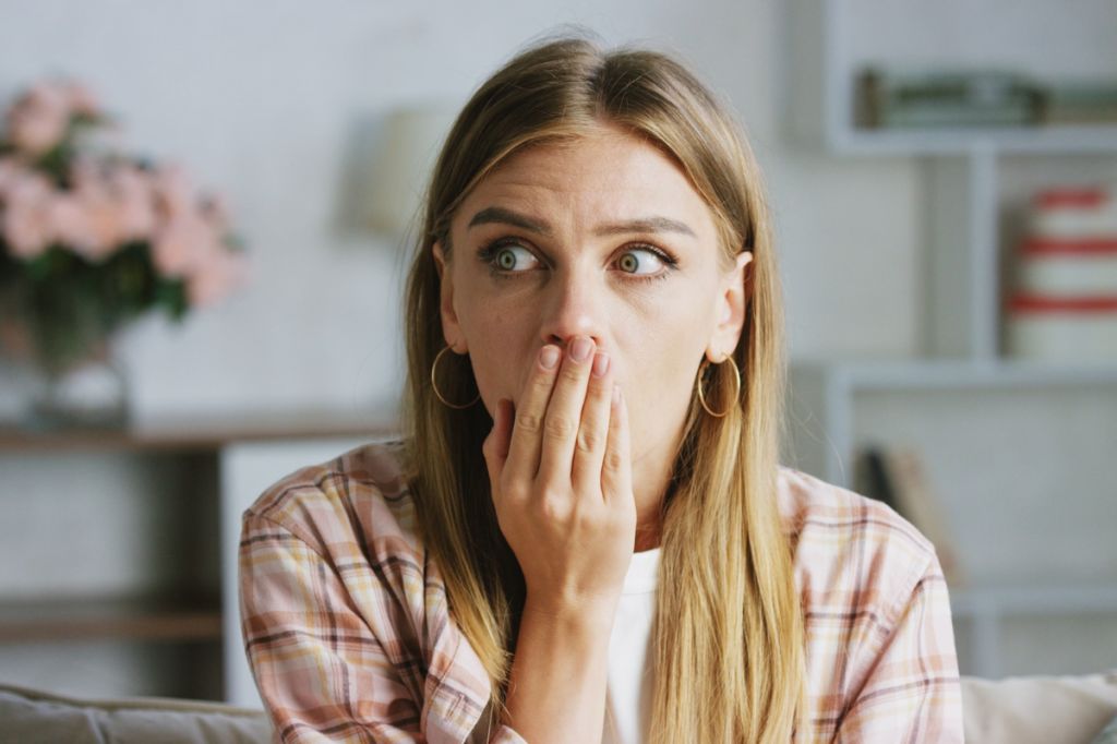 woman looks shocked and upset, covers hand with mouth