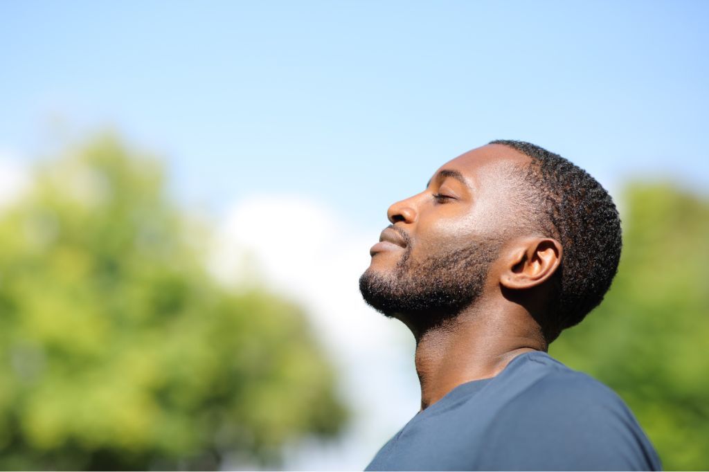 man takes deep breath outside in nature, eyes closed and gently smiling