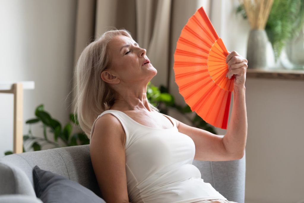 older woman sits on sofa fanning herself due to heat