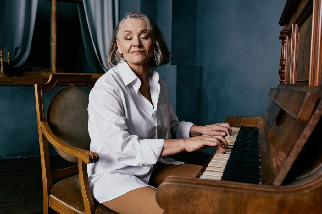 Mature woman sits at antique piano with her eyes closed playing music