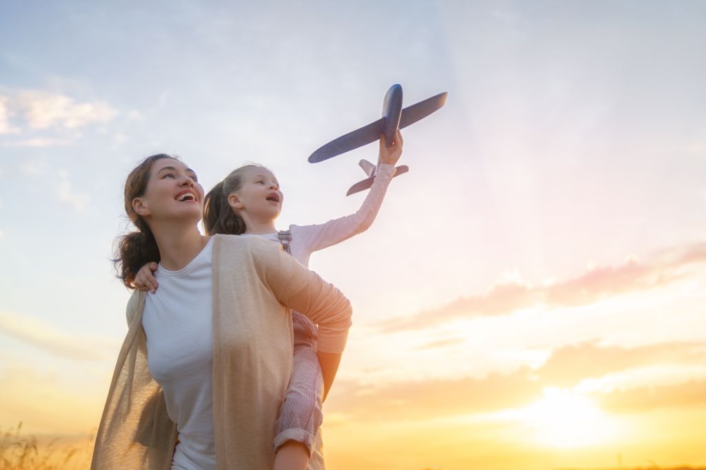 mum gives daughter a piggyback, she is making her toy plane fly through the sky