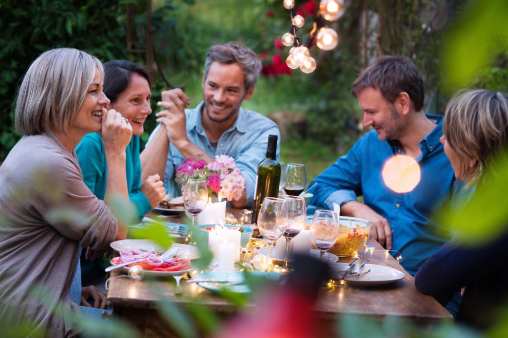 group of adults sit around a summer dining table outside happily chatting