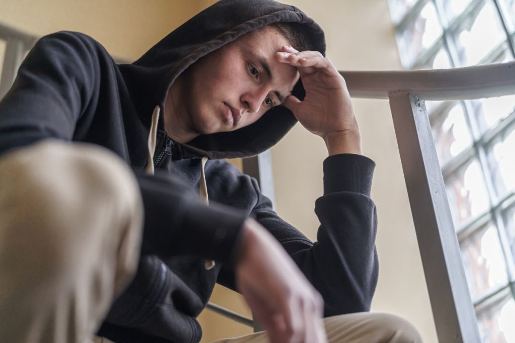 man looks at floor, holding head in his hand