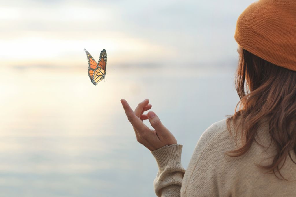 woman looks out to see as a butterfly is about to land on her outstretched finger