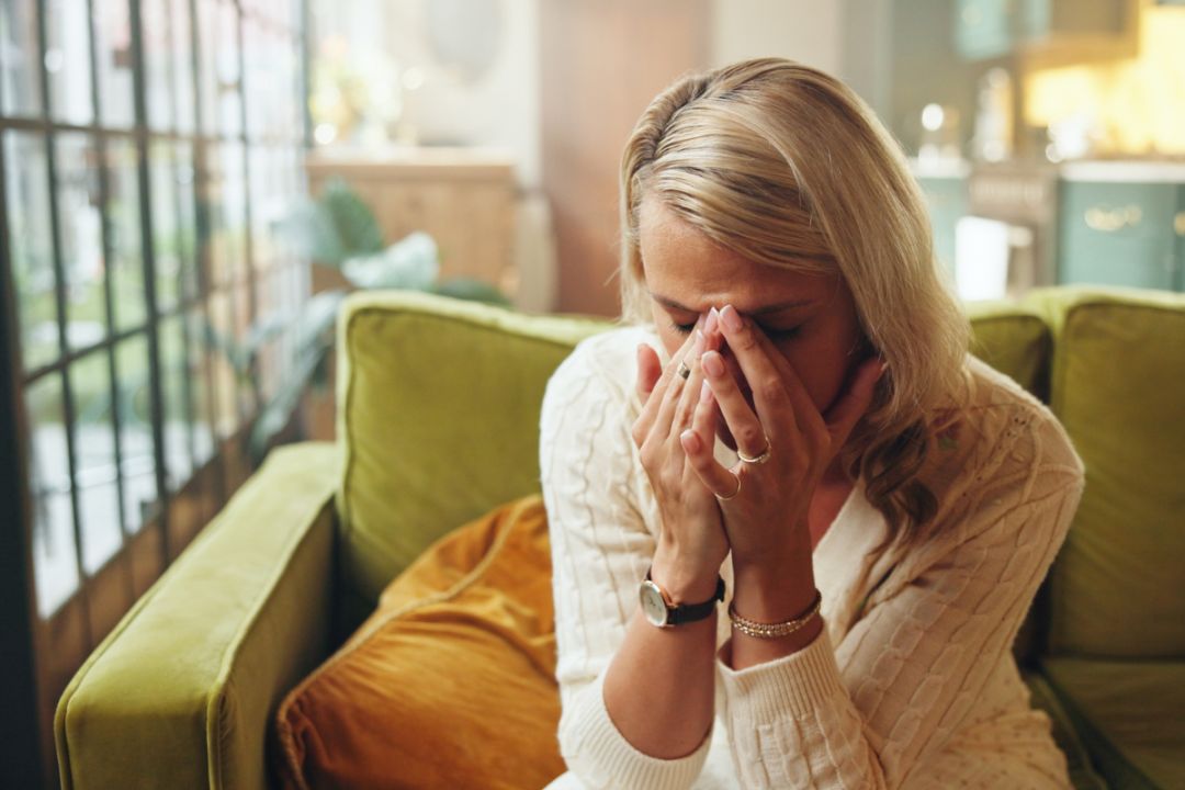 woman sits on sofa with hands covering her face