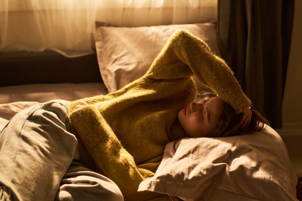 woman ling in bed in a jumper, struggling with mental health