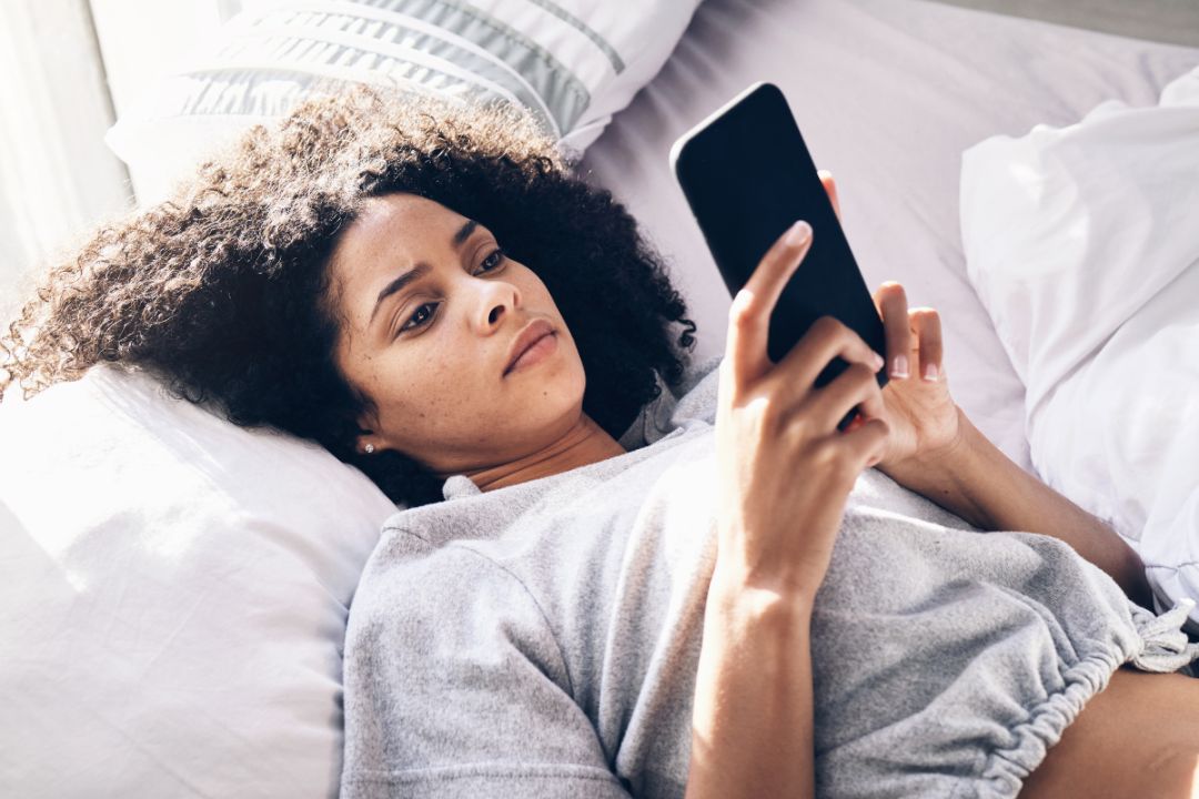 young woman lies on bed and looks worried at phone