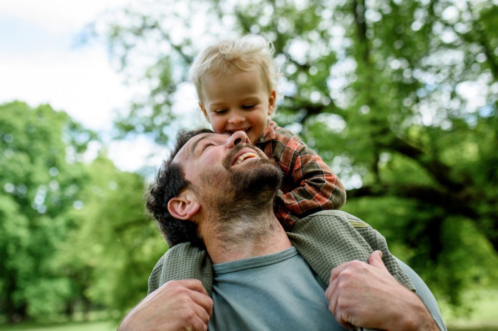 happy dad looks up to young son sitting on his shoulders