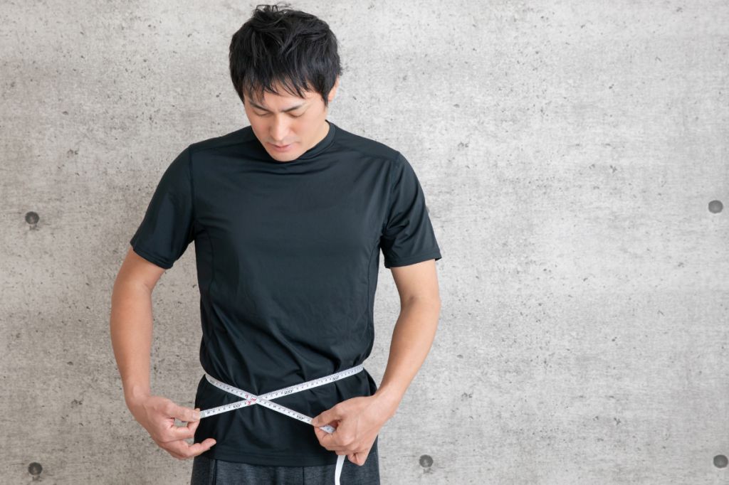 young man in black sporty t-shirt uses tape measure around waist