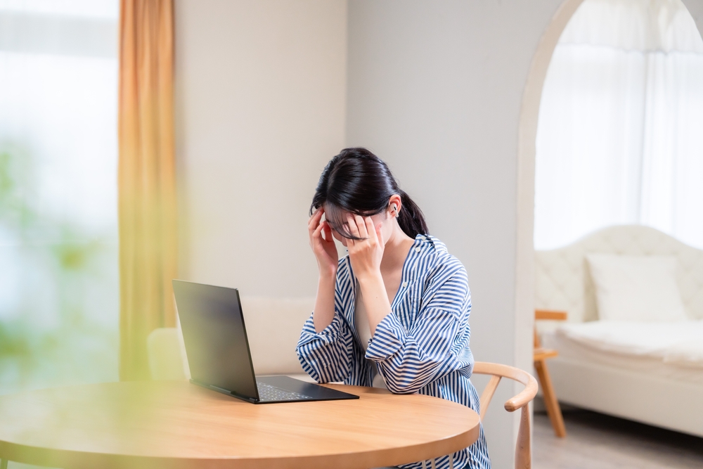 woman showing signs of burnout at work, she sits at a table with her laptop open and her head in her hands
