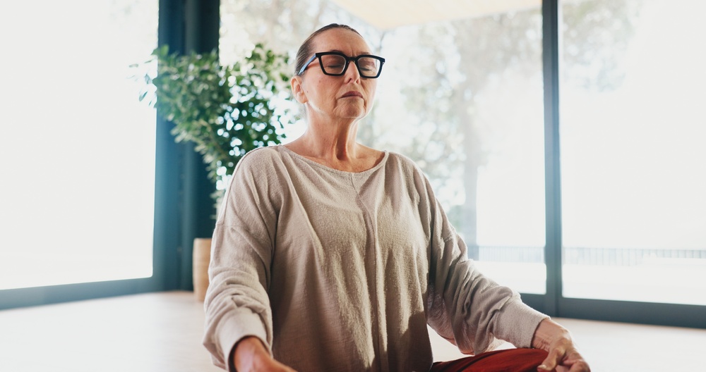 woman sat on the floor at home with eyes closed, meditating and being mindful in the present moment to clear brain fog