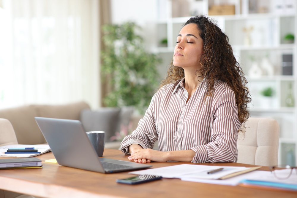 woman sat at office desk feeling stressed, she is taking deep breaths