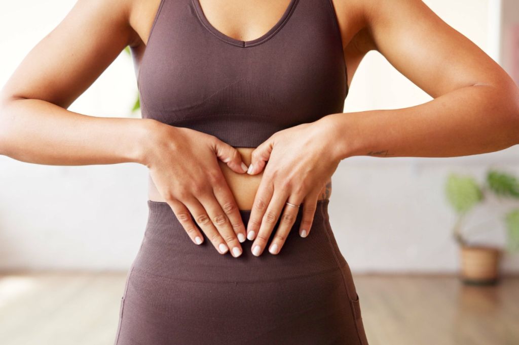 woman holds hands in front of stomach making heart shape