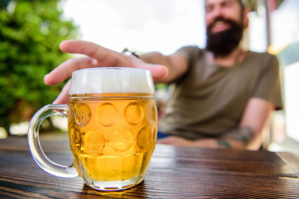 man sits at table in beer garden, reaches for cold glass of lager